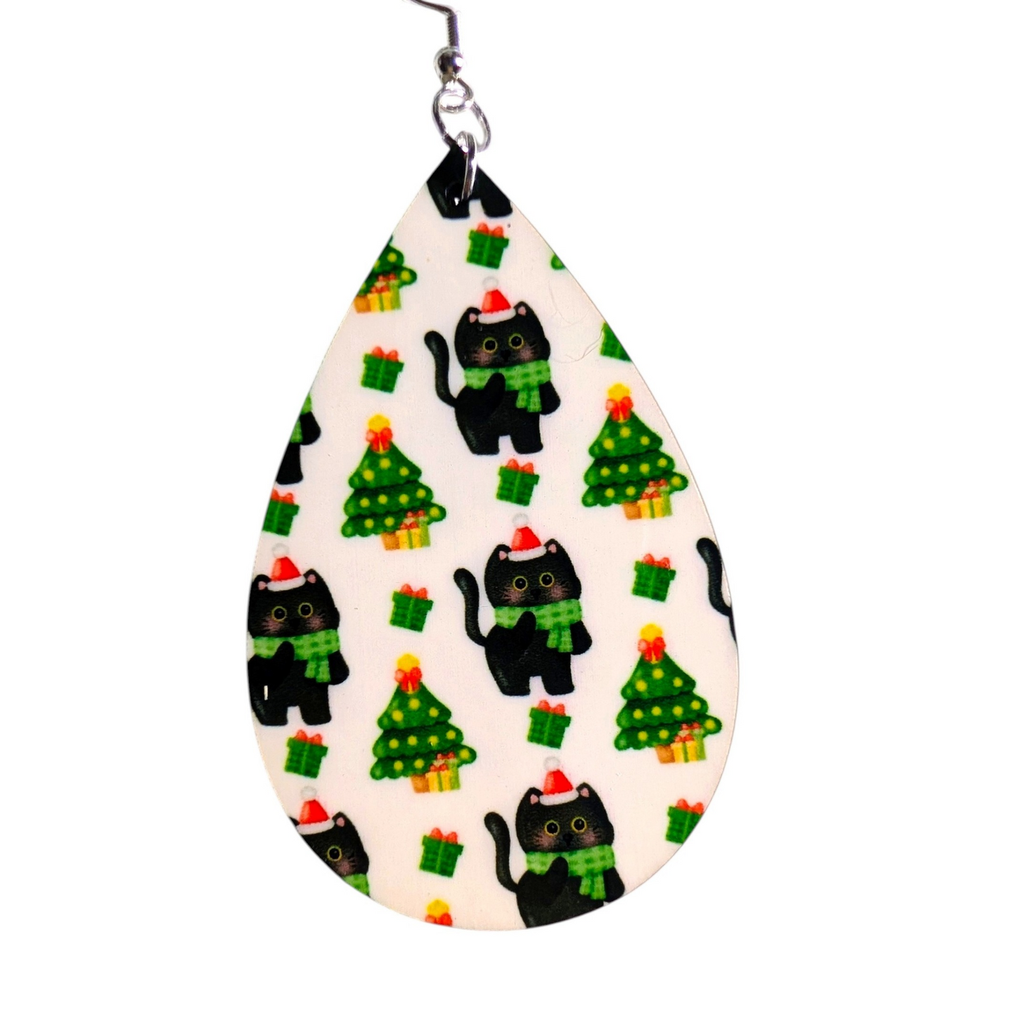A teardrop-shaped earring with a white background and a repeating pattern of black cats wearing green scarves and Santa hats, alongside green Christmas trees with yellow and red presents, hanging from a silver metal hook.