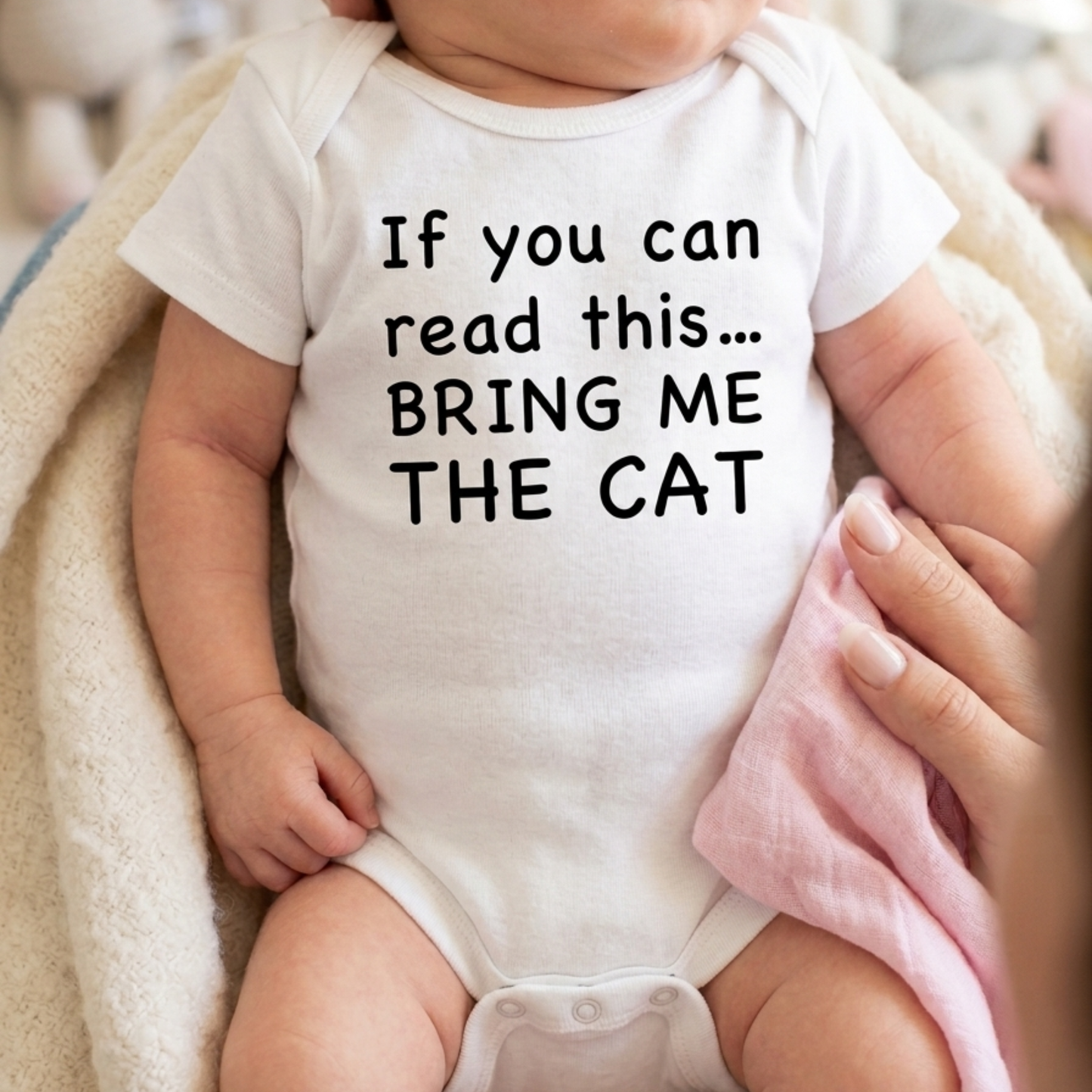 Baby wearing a white onesie with text 'If you can read this... BRING ME THE CAT' held by a person.