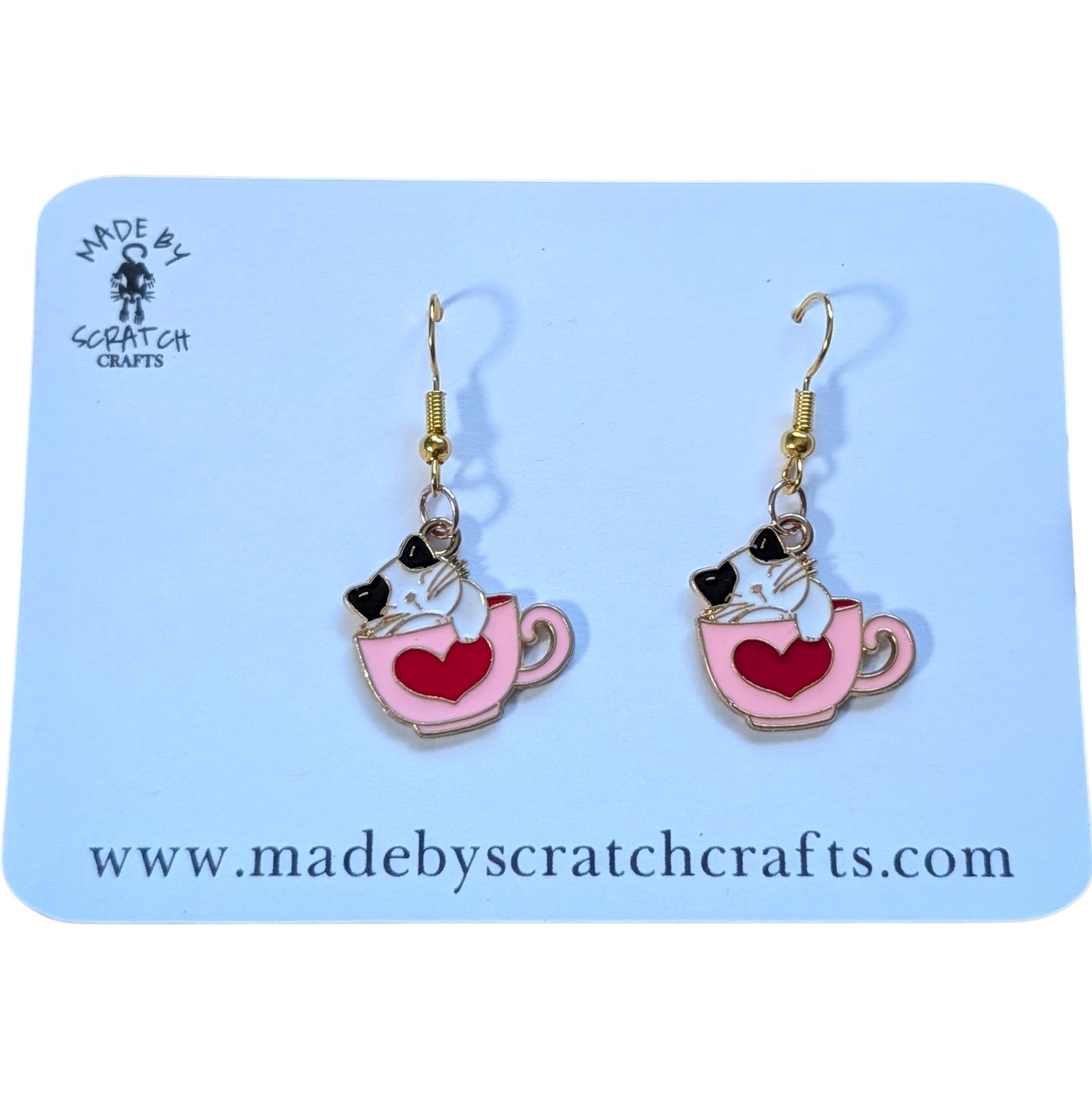 Earrings with a cat design in a teacup on a 'Made by Scratch Crafts' card.