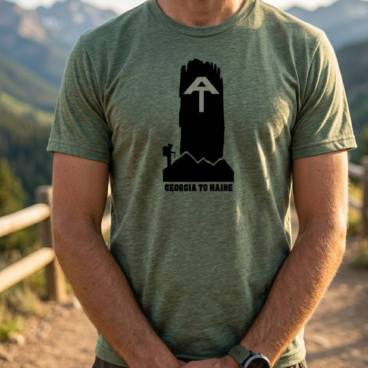 Person wearing a green t-shirt with a black graphic design in a mountainous landscape