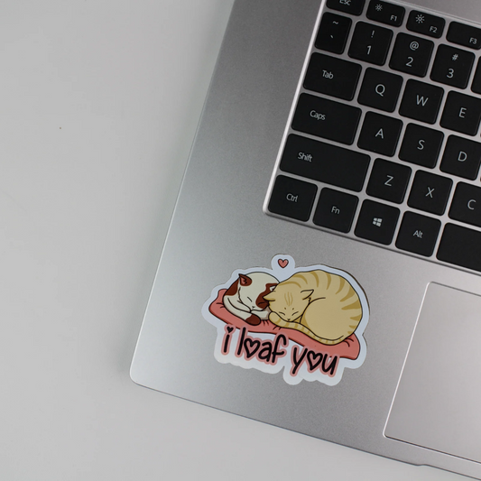 Laptop with a sticker of two cats and 'I loaf you' text on a white background