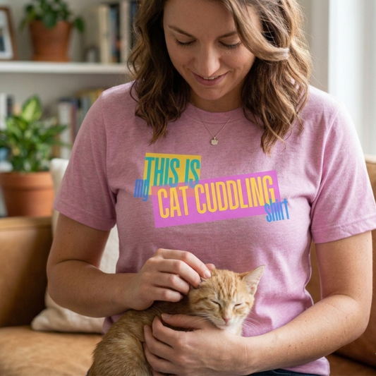 Woman wearing a pink t-shirt with colorful text that says "This is my Cat Cuddling Shirt" holding a cat indoors.