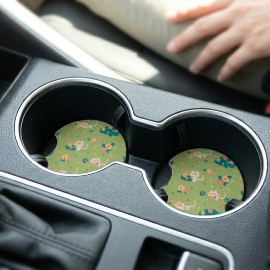 Car cup holder with floral and cat coasters and a hand reaching towards the console.
