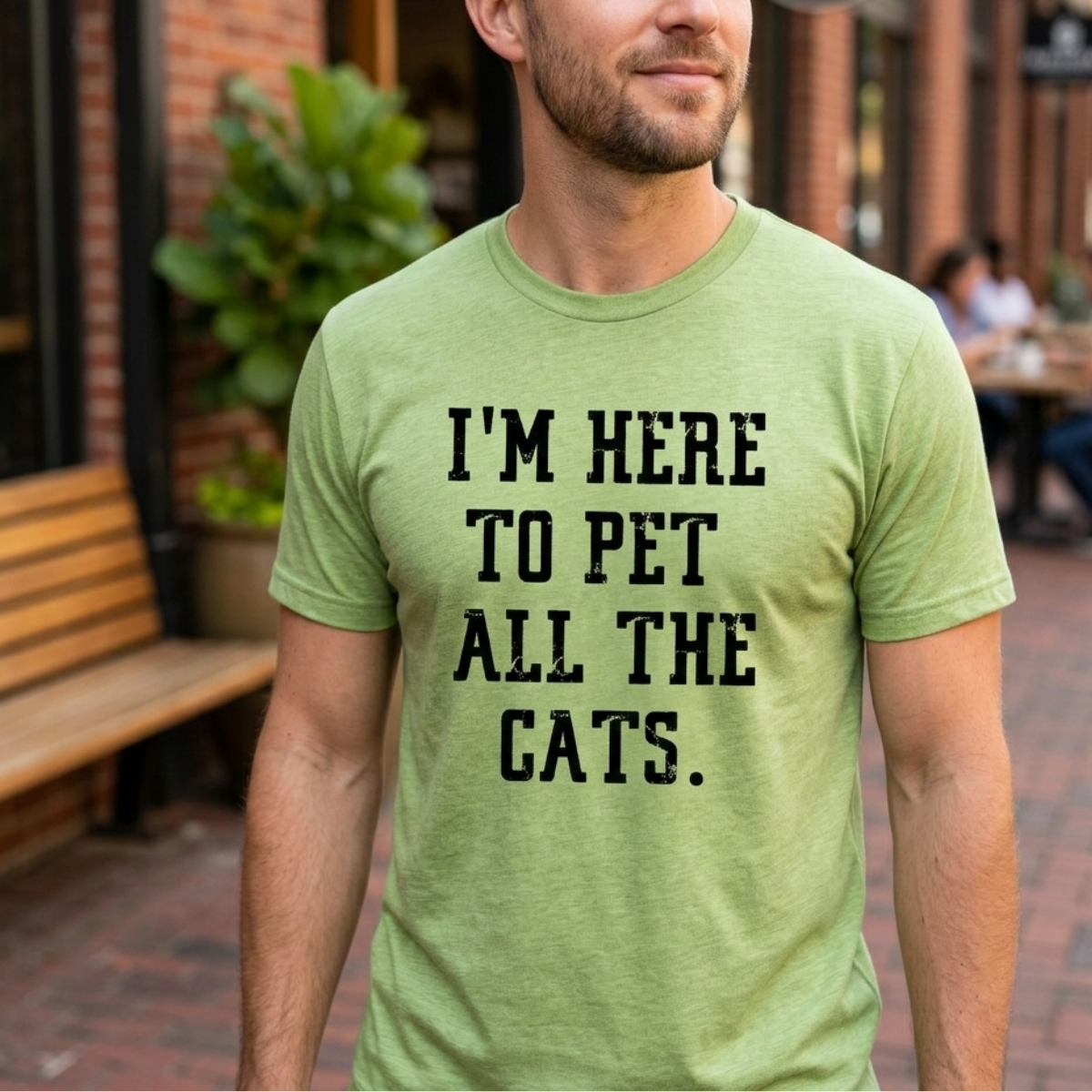 Man wearing a green t-shirt with text 'I'm here to pet all the cats' outdoors.