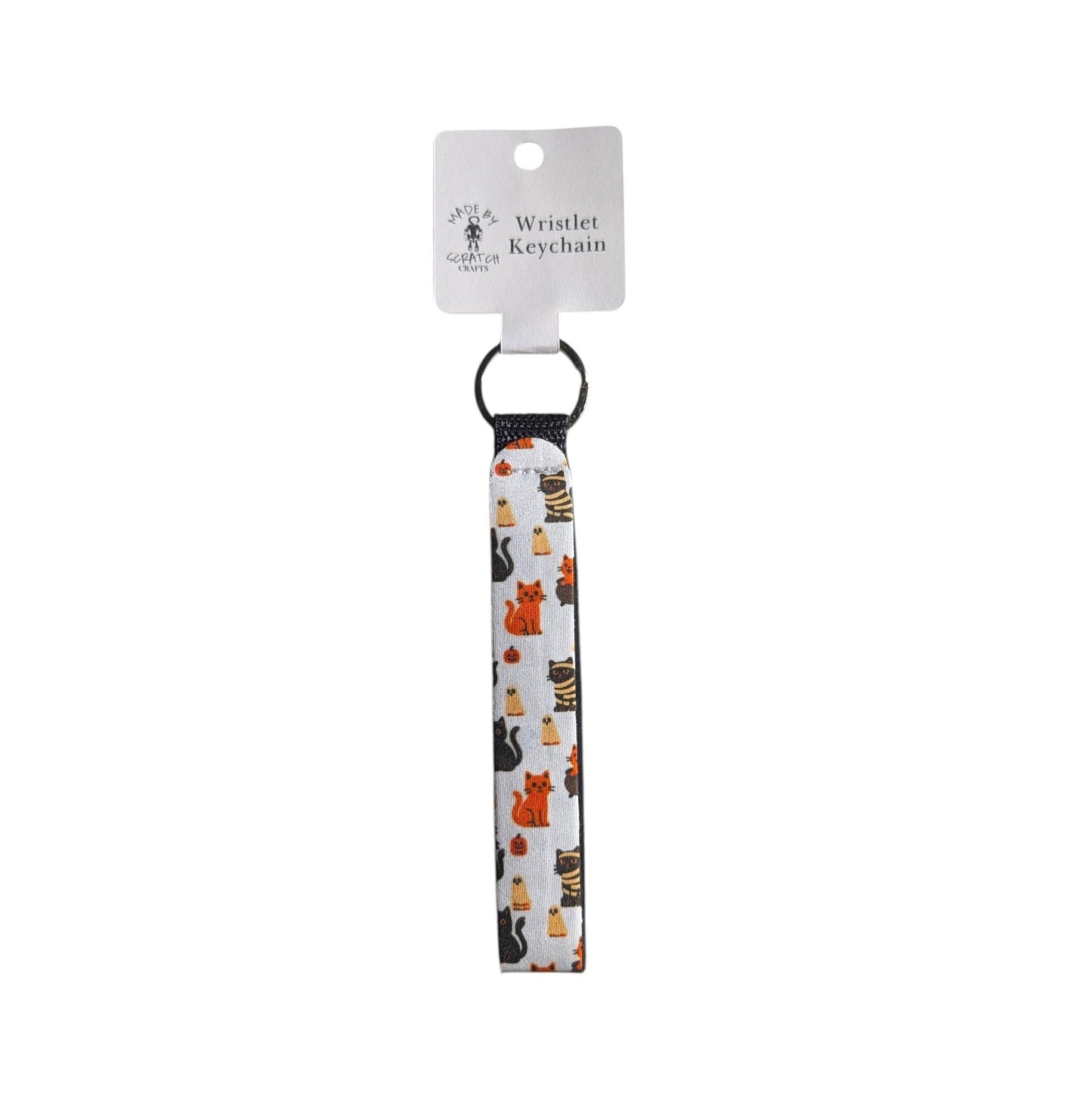 A white wristlet keychain with a black elastic loop and a printed pattern of various cartoon cats in orange, black, and white. It is attached to a white cardboard hanger tag printed with the text 'Wristlet Keychain' and the brand Made By Scratch Crafts.