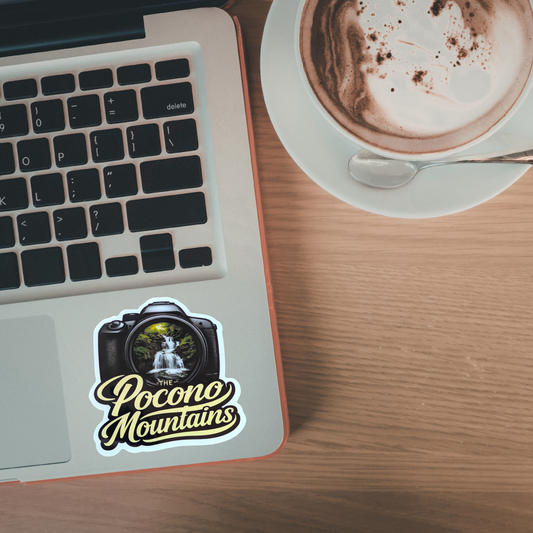 Laptop with 'Pocono Mountains' sticker next to a cup of coffee on a wooden table