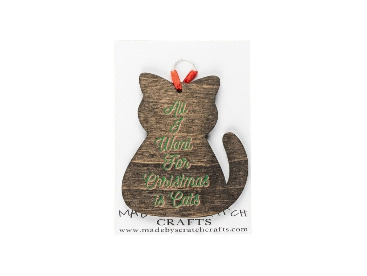 A rustic wooden cat-shaped Christmas ornament with the phrase 'All I Want For Christmas is Cats' in green script, hanging from a red ribbon on a white background.