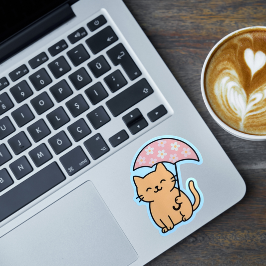 Laptop with a cat sticker holding an umbrella, next to a cup of coffee on a wooden surface.