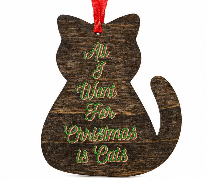 A dark brown wooden cat-shaped Christmas ornament with the phrase 'All I Want For Christmas is Cats' written in green cursive text outlined in red, hanging from a red ribbon on a white background.