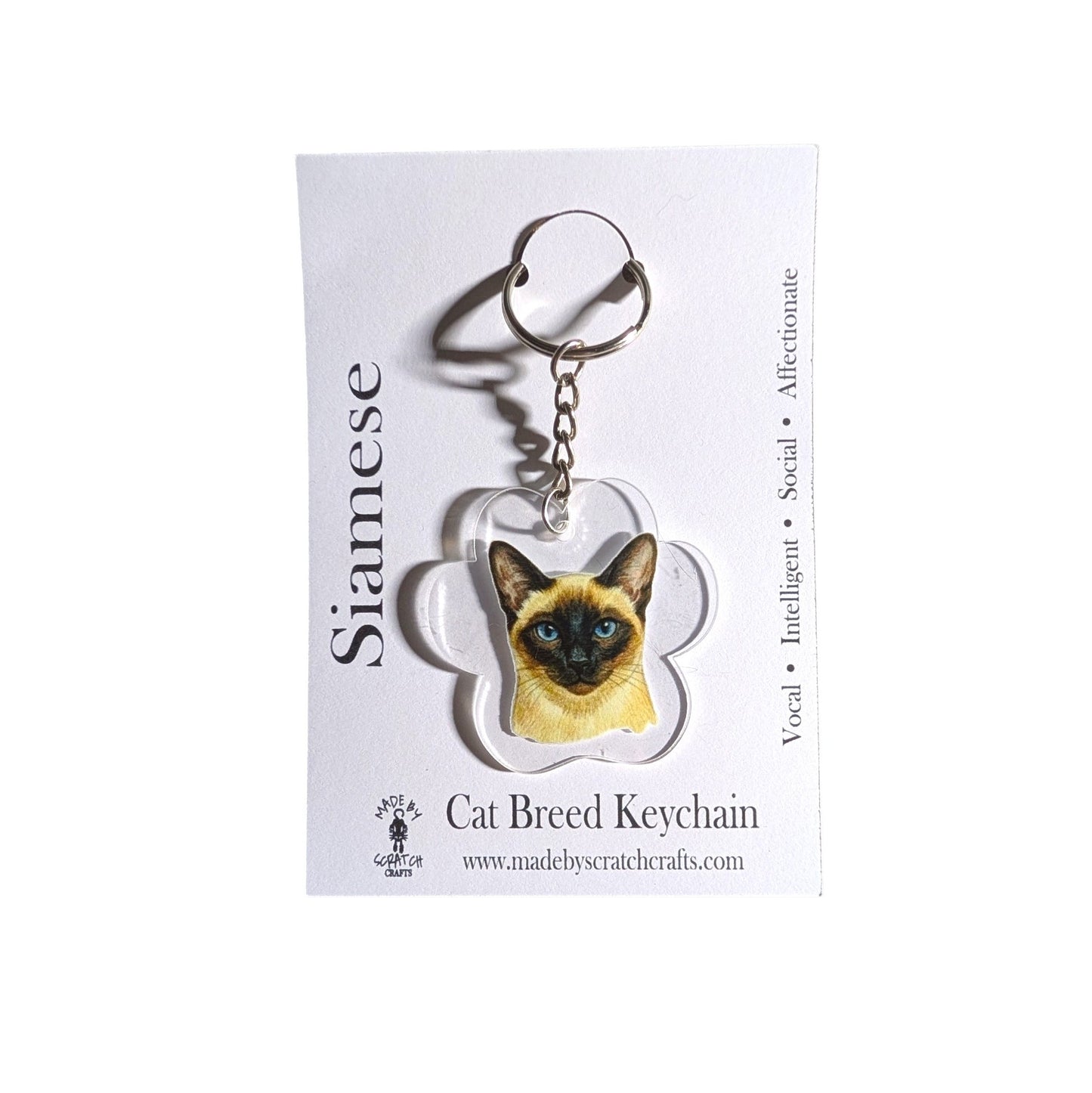 A Siamese cat breed keychain charm displayed on its white backing card. The keychain features a detailed illustration of a Siamese cat inside a paw print shaped acrylic piece attached to a silver split ring.