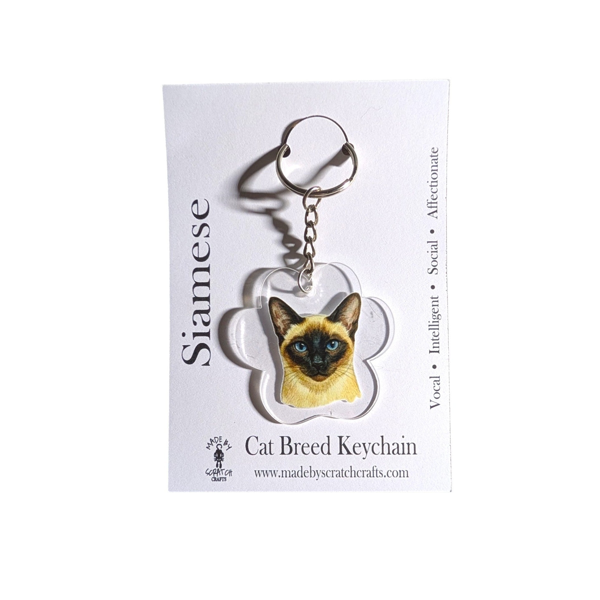 A Siamese cat breed keychain charm displayed on its white backing card. The keychain features a detailed illustration of a Siamese cat inside a paw print shaped acrylic piece attached to a silver split ring.