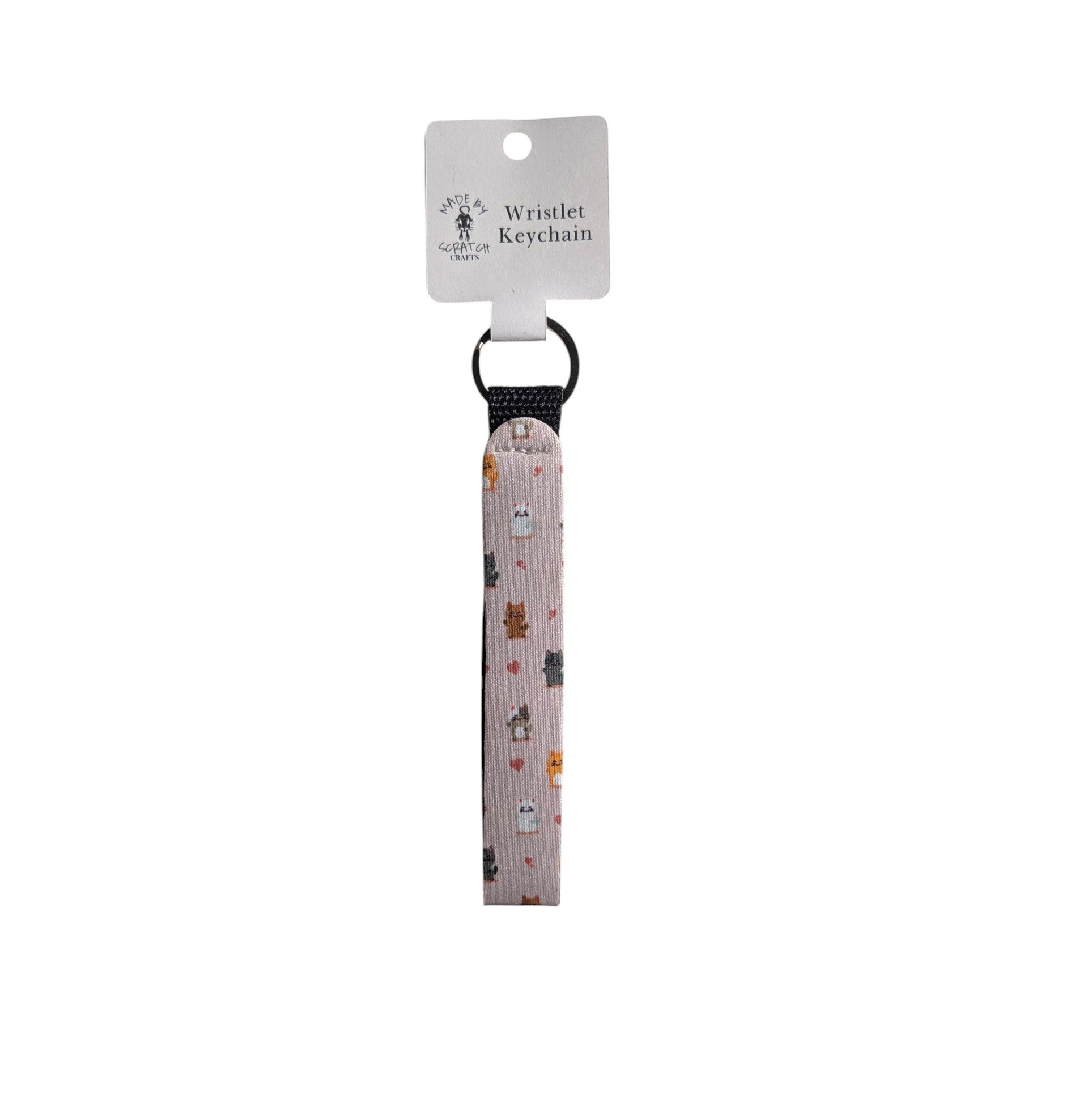 A fabric wristlet keychain with a light pink background and a cute cat pattern, attached to a key ring and a white paper hanger tag.