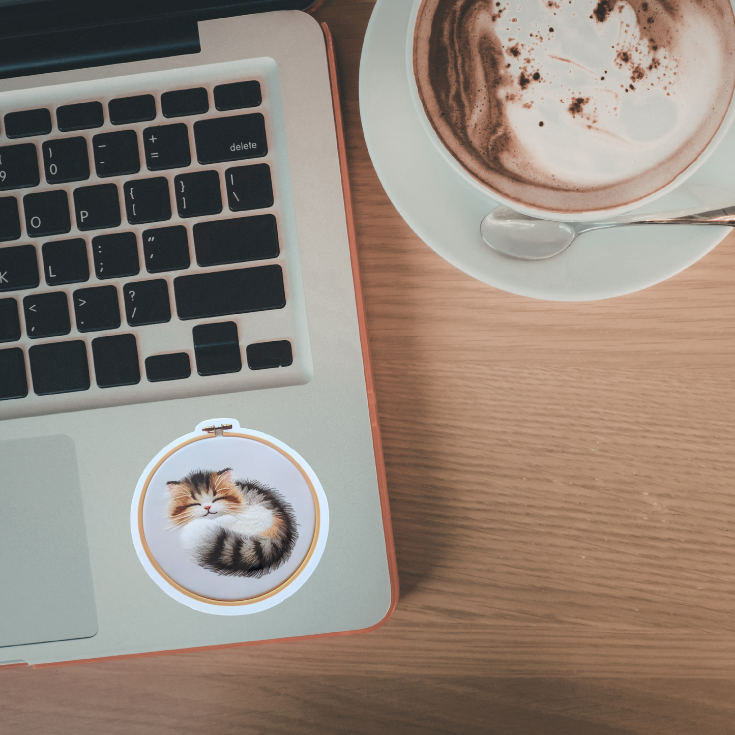 Laptop with a cat sticker on a wooden desk next to a cup of coffee.