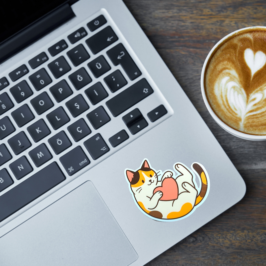 Laptop with a calico cat sticker on the palm rest area next to a cup of coffee.