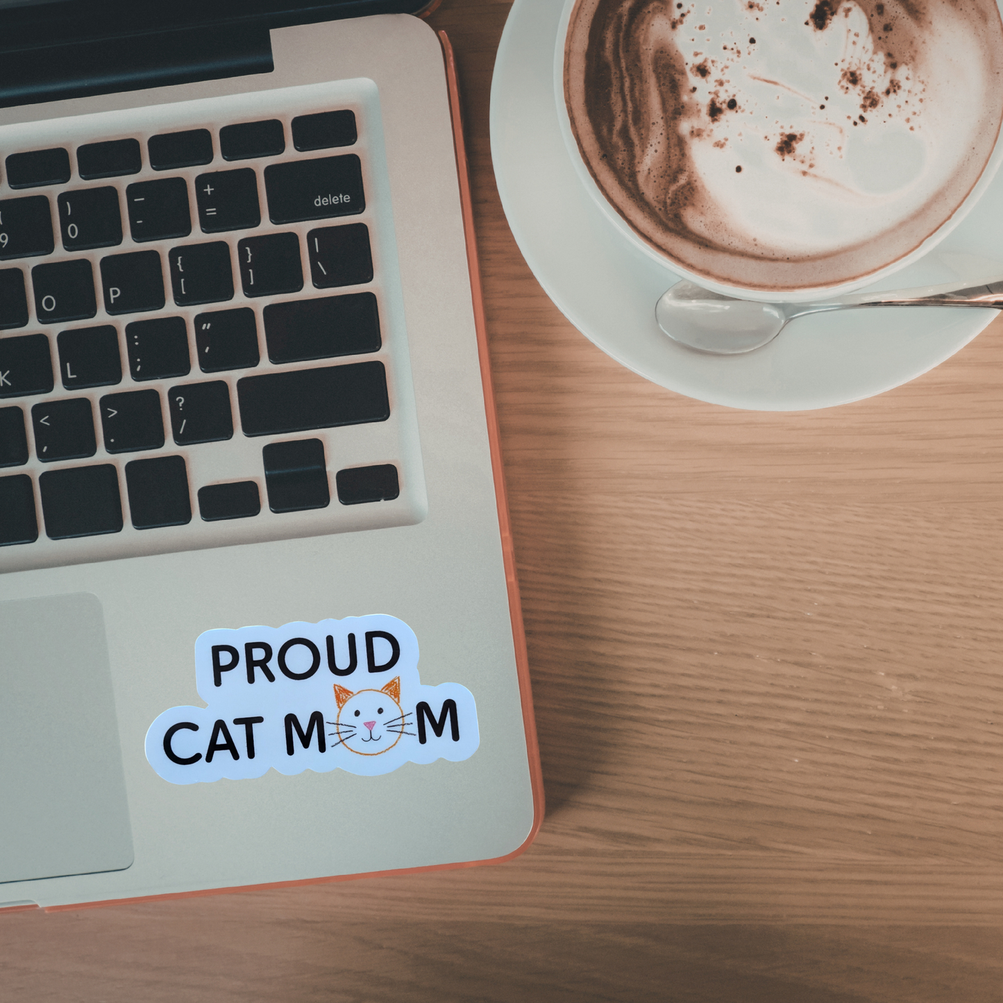 Laptop with 'Proud Cat Mom' sticker next to a cup of coffee on a wooden table