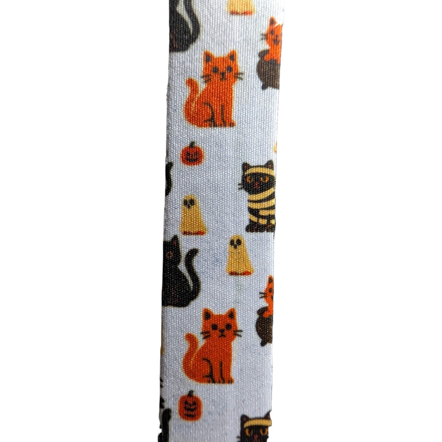 A close-up of a white fabric strap featuring a repeating Halloween pattern of orange, black, and yellow cats, pumpkins, and ghosts.