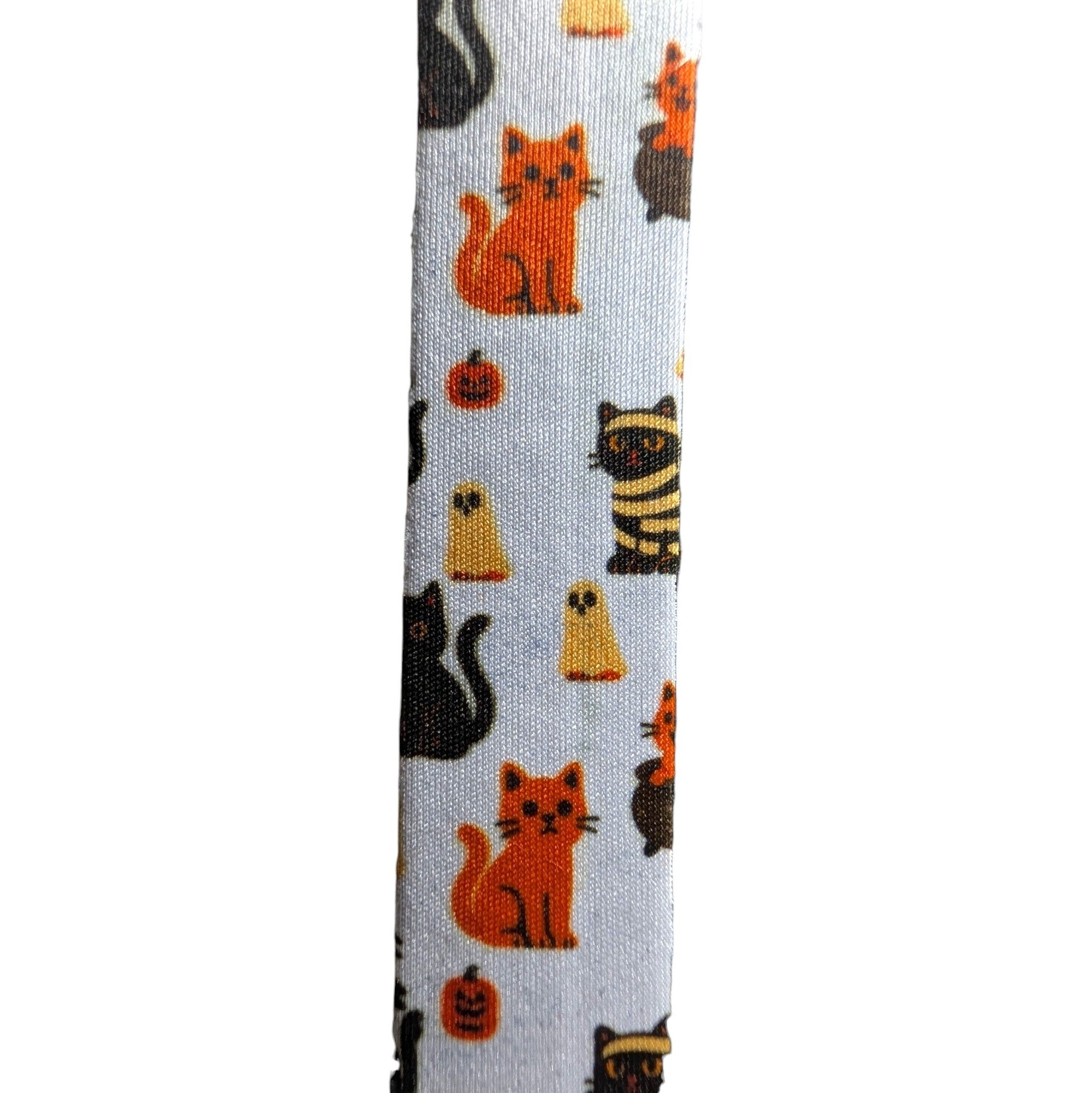 A close-up of a white fabric strap featuring a repeating Halloween pattern of orange, black, and yellow cats, pumpkins, and ghosts.