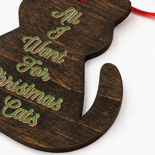 A dark brown wooden Christmas ornament shaped like a cat, featuring the phrase 'All I Want For Christmas Cats' in green and red glittery script, with a red hanging ribbon.