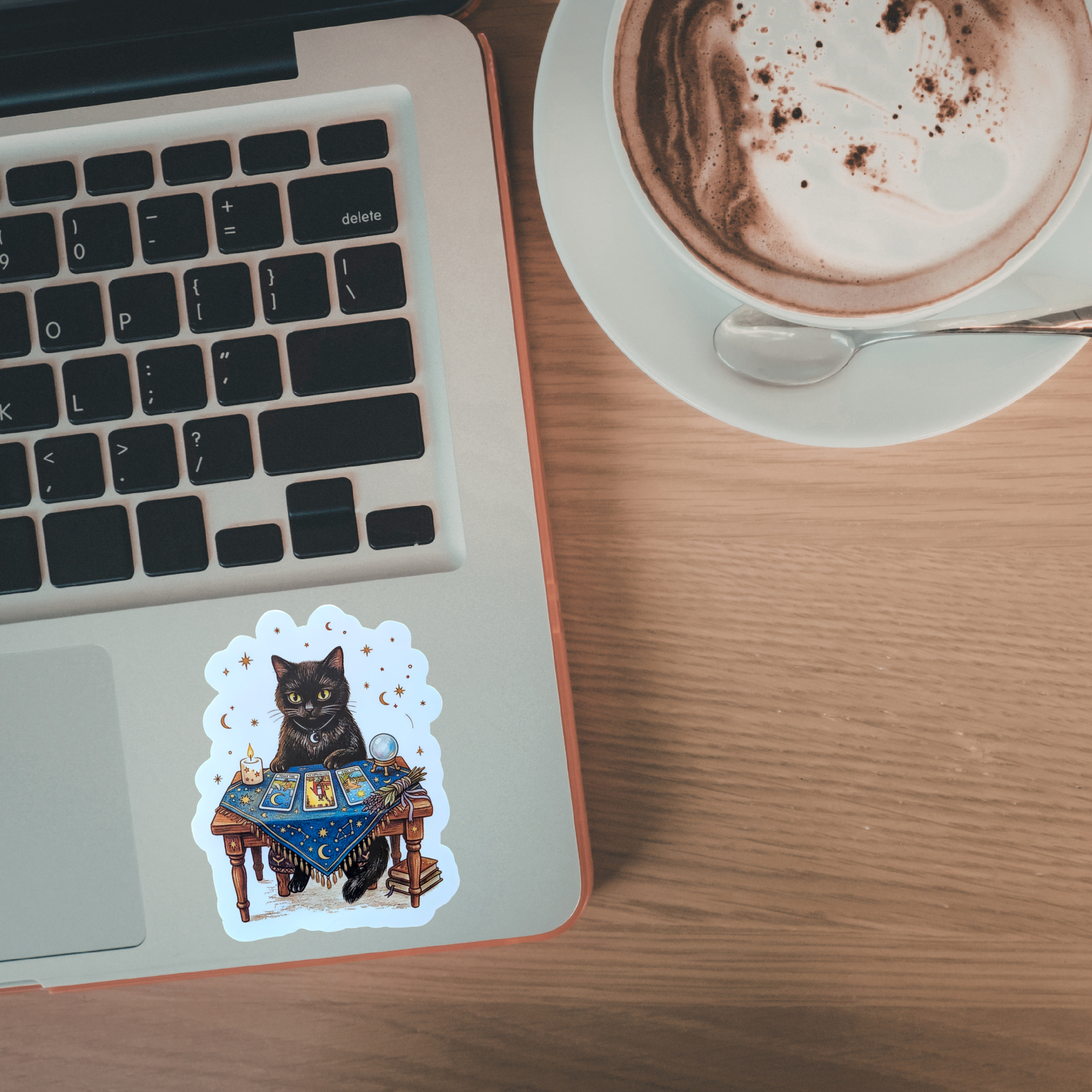 Laptop with a cat sticker on a wooden desk next to a cup of coffee.