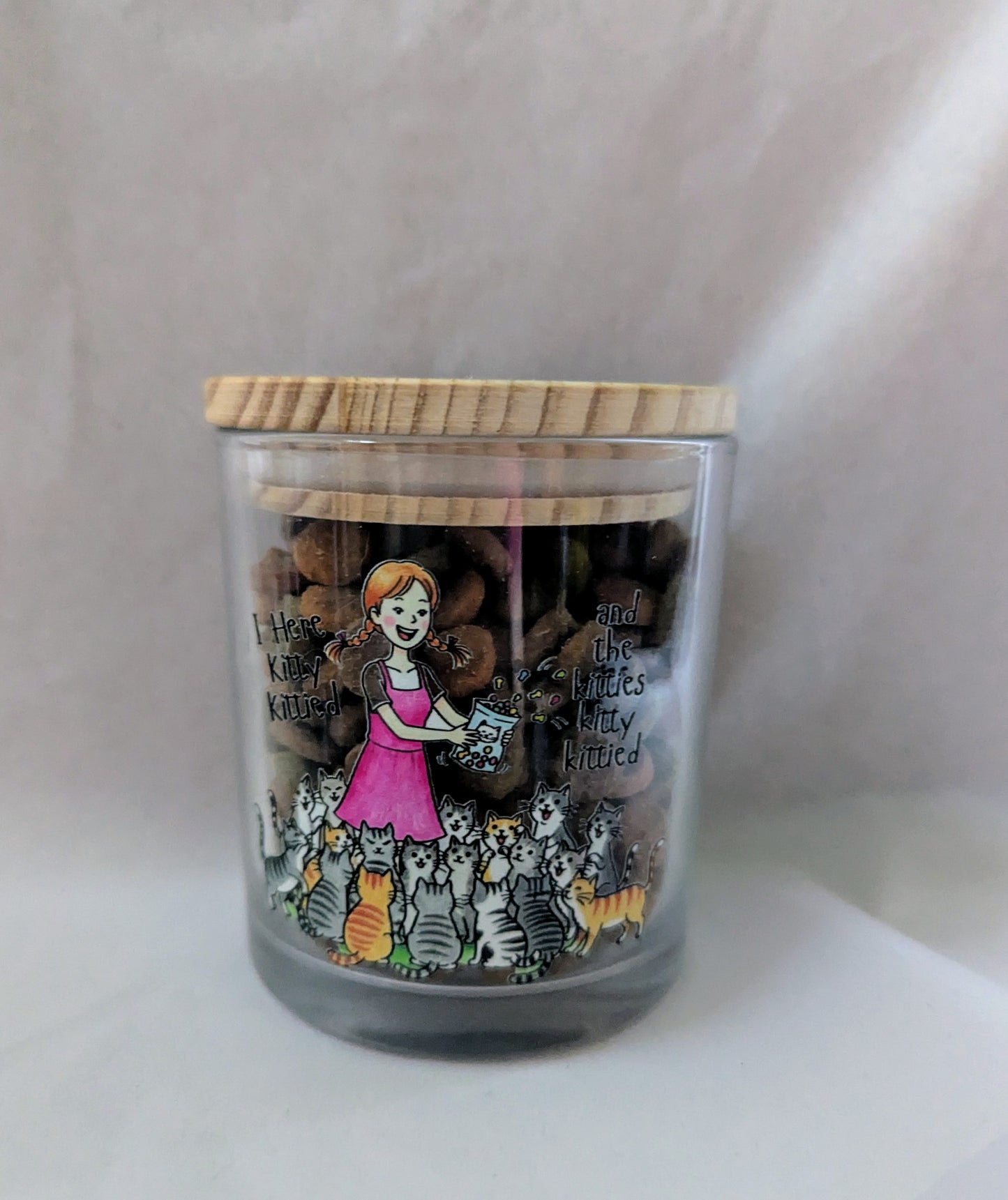 Decorative jar with a wooden lid featuring illustrations of a girl with cats on a white background