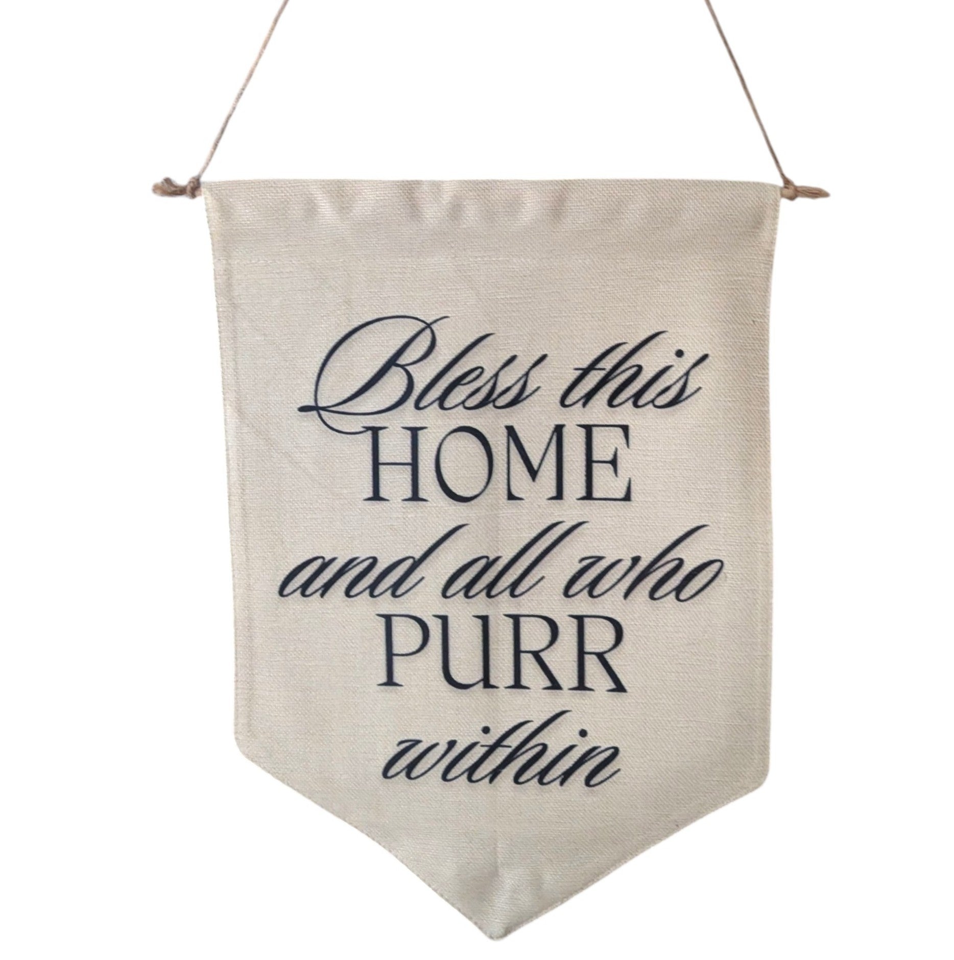 A beige linen pennant banner with the phrase 'Bless this HOME and all who PURR within' in dark navy lettering, hanging from a jute twine string against a plain white background.