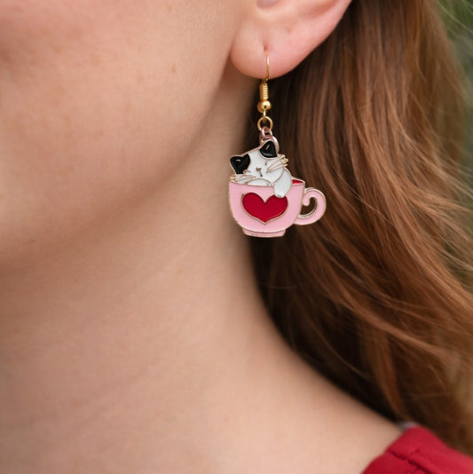 Earring with a cat in a pink teacup design worn by a person.