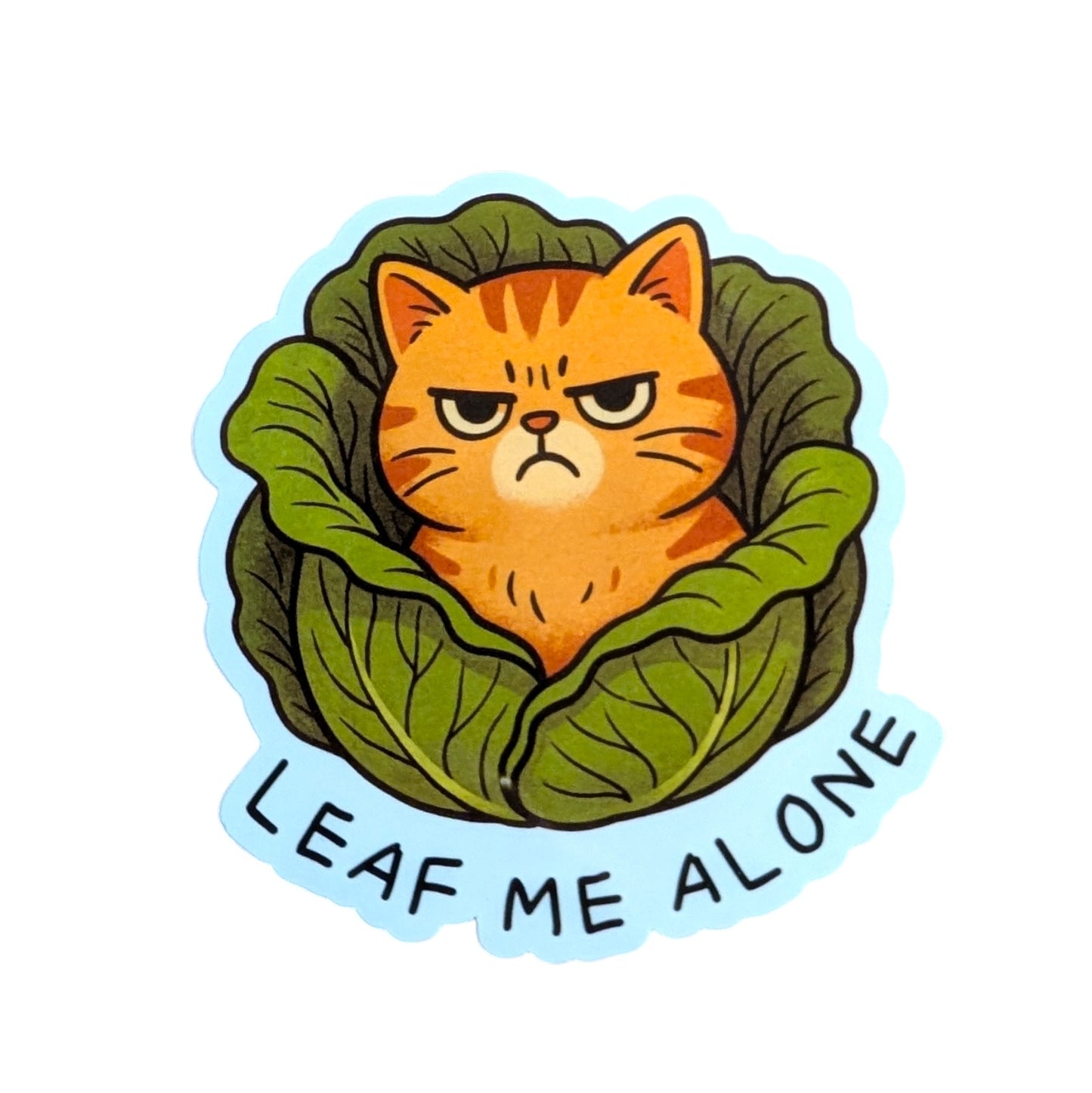 Sticker with a cat inside a cabbage leaf and 'Leaf Me Alone' text on a white background