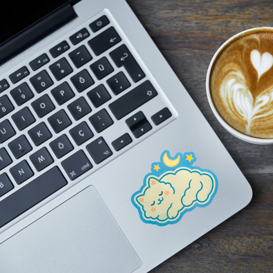 Laptop with a sticker of a cat on a cloud, next to a cup of coffee on a wooden surface.