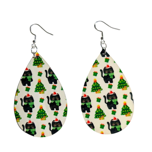 A pair of teardrop-shaped dangle earrings with a Christmas-themed pattern of black cats wearing red Santa hats and scarves, green Christmas trees, and gift boxes, suspended from silver fishhook wires.