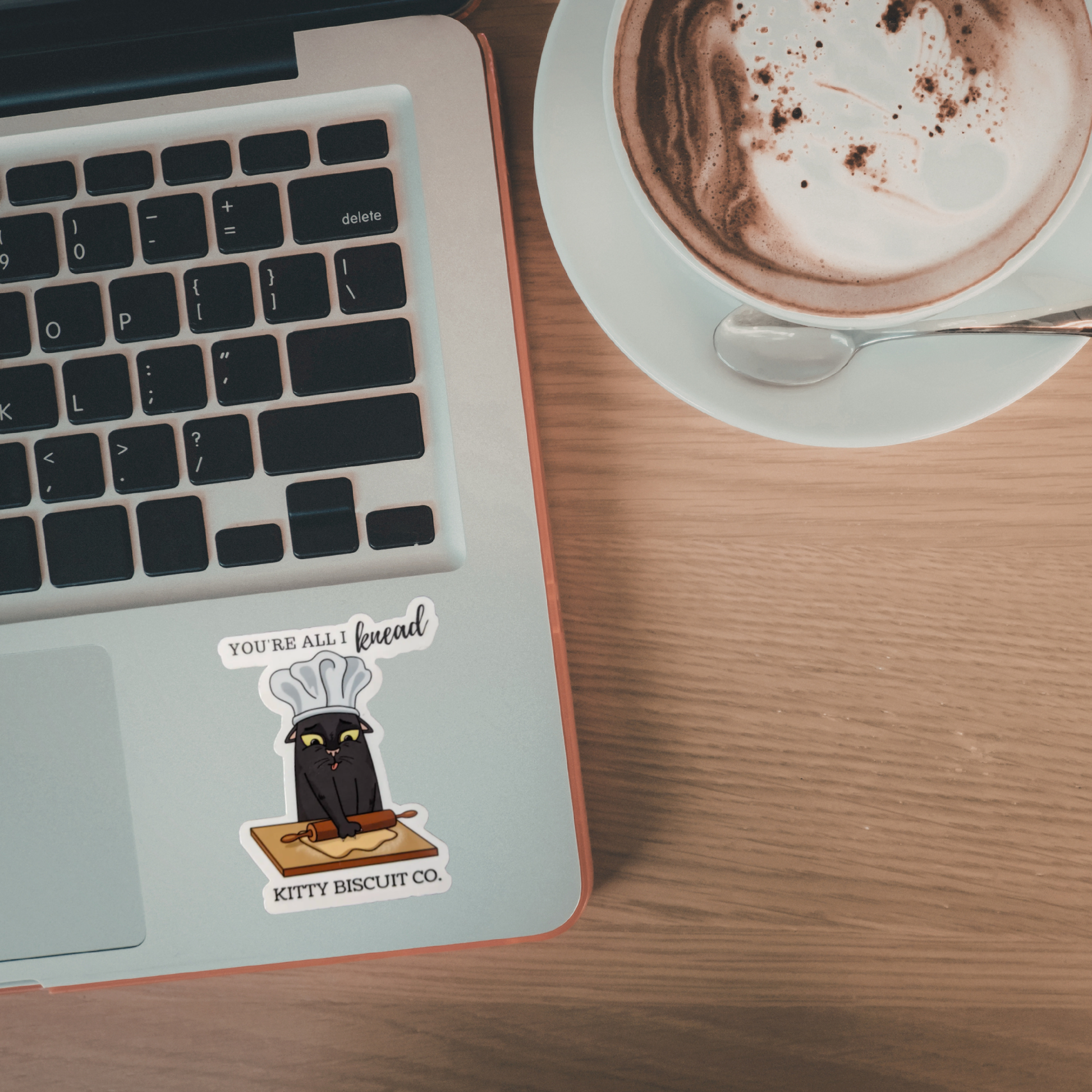 Laptop with a sticker on a wooden desk next to a cup of coffee