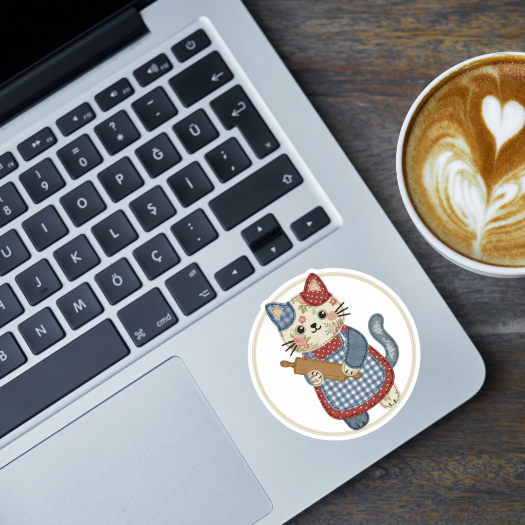 Laptop with a sticker of a cat wearing a chef's hat and apron, next to a cup of coffee on a wooden surface.