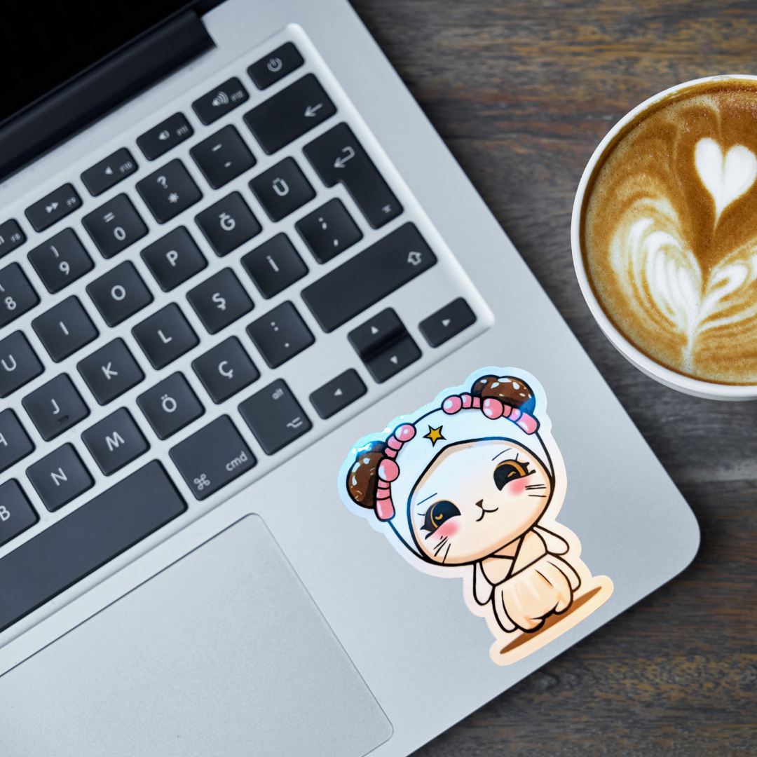 Laptop with a cute cartoon space princess cat sticker on the keyboard next to a cup of coffee.