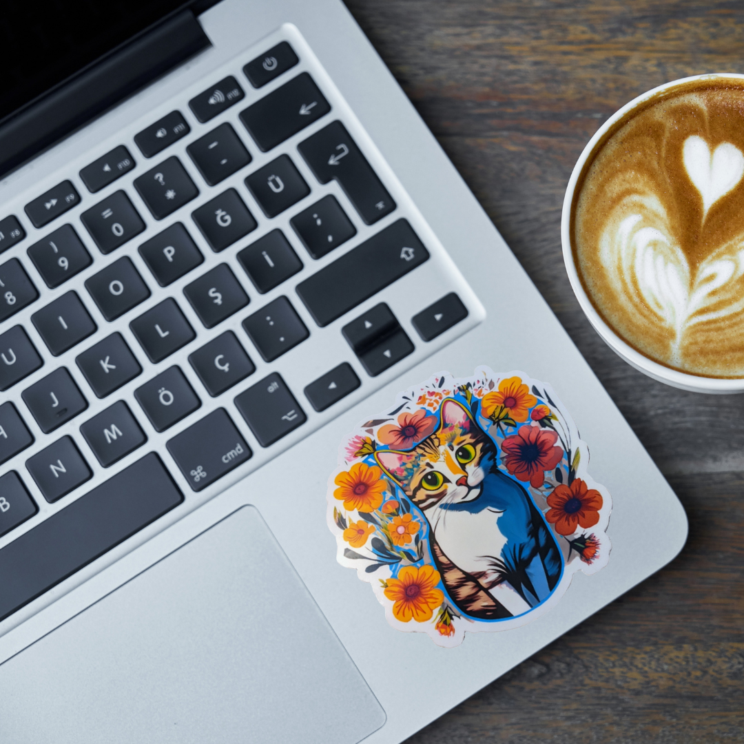 Laptop with a cat and flower sticker on a wooden desk next to a cup of coffee.