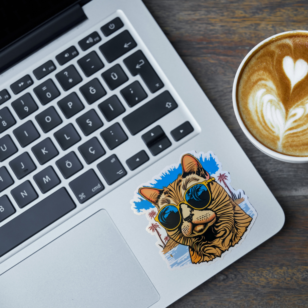 Laptop with a cat sticker wearing sunglasses on a wooden desk next to a cup of coffee.