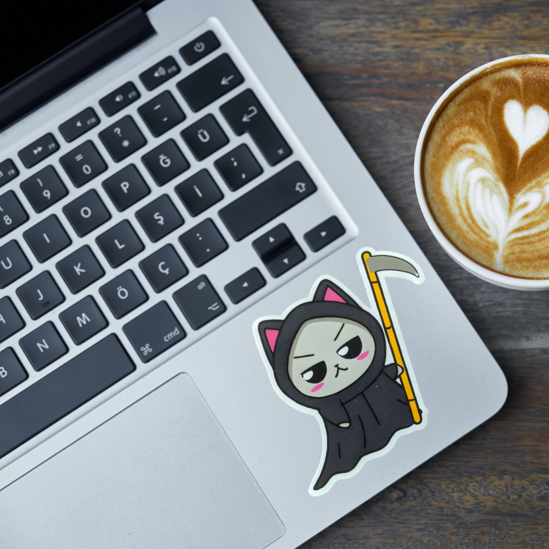 Laptop with a sticker of a cartoon character holding a scythe next to a cup of coffee on a wooden surface.