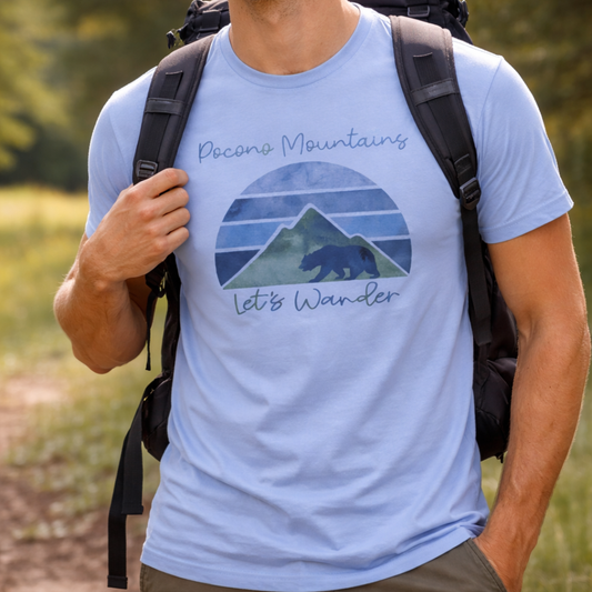 Person wearing a light blue t-shirt with a mountain and bear graphic and text 'Pocono Mountains Let's Wander' outdoors.
