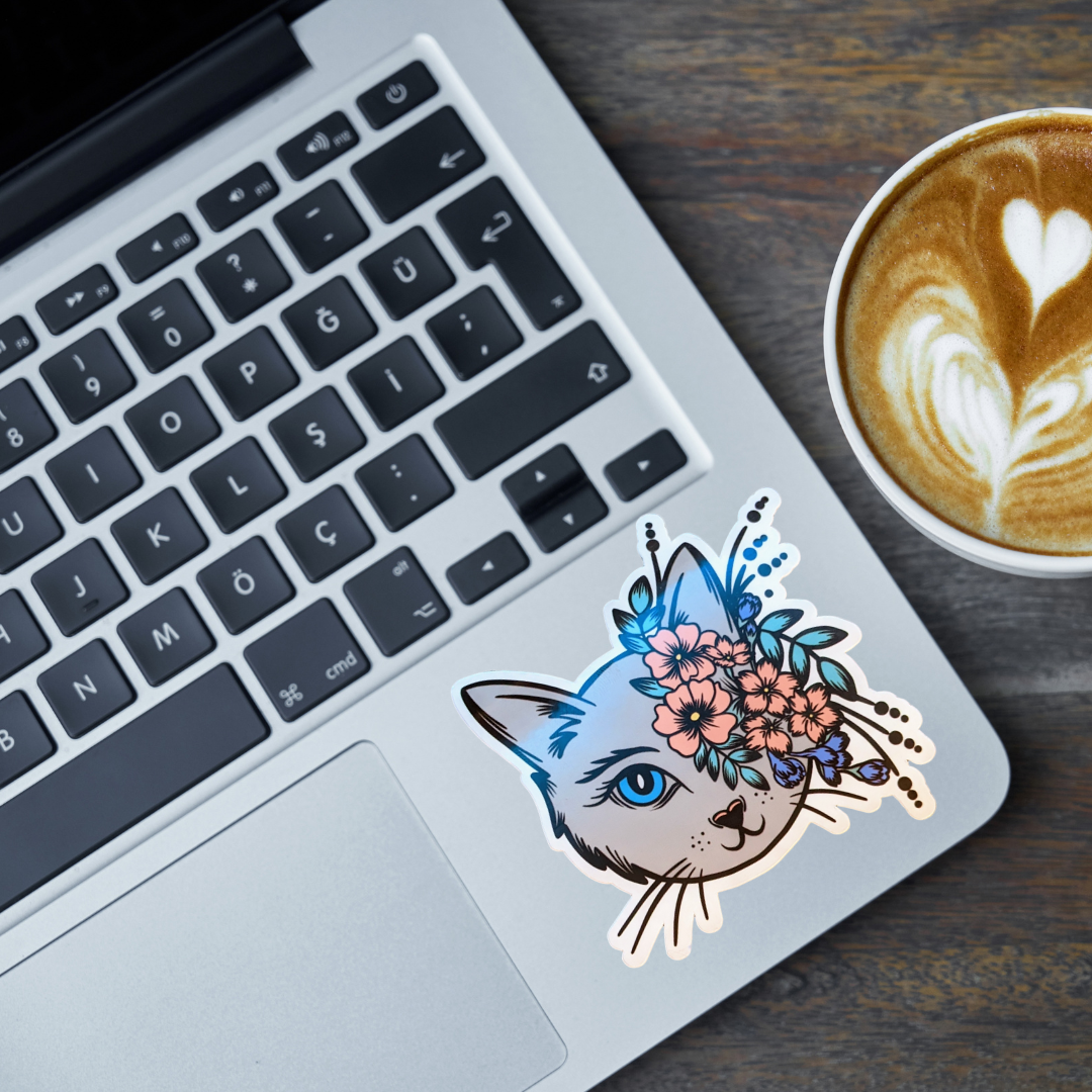 Laptop with a decorative cat sticker on the palm rest area, next to a cup of coffee.