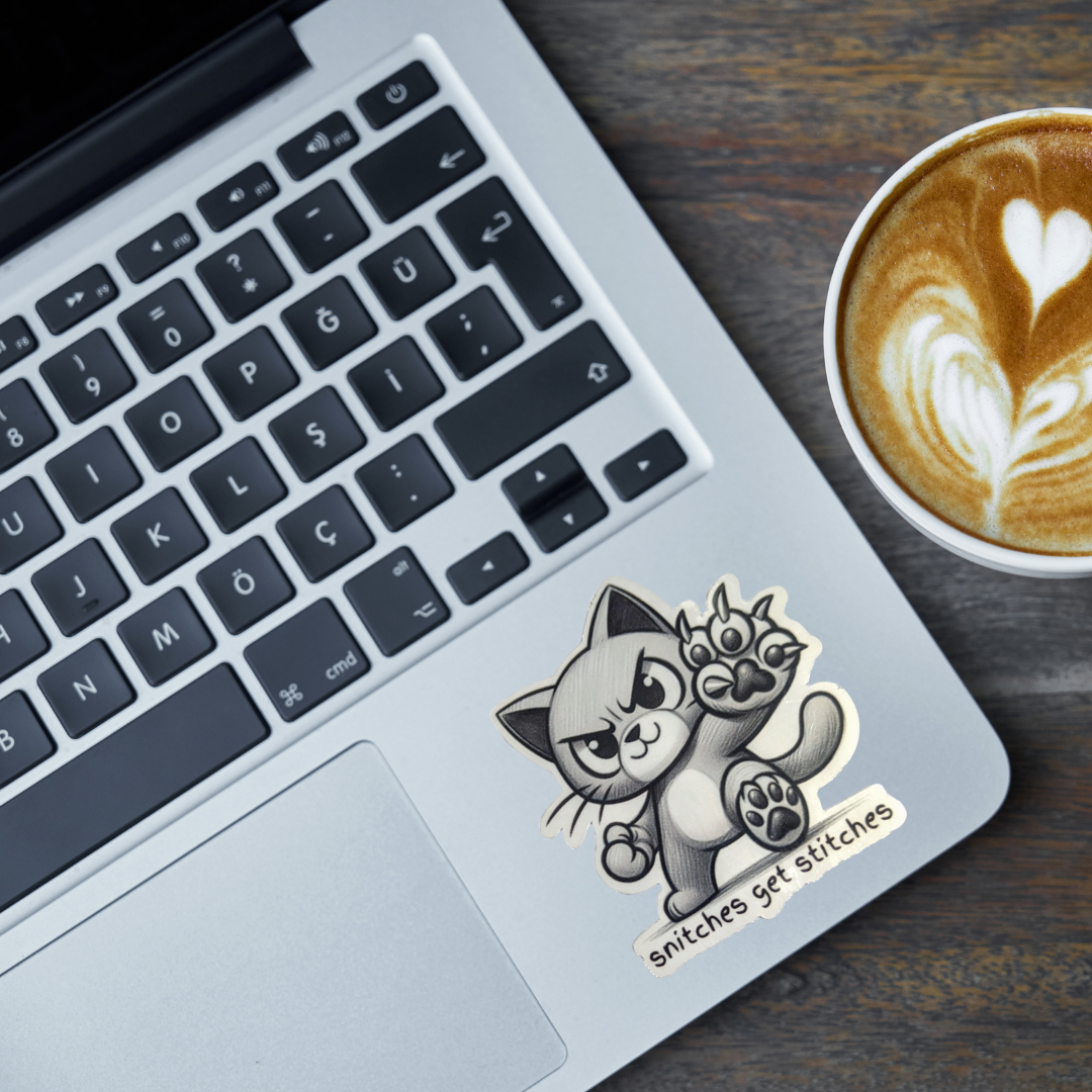 Laptop with a sticker of a cat holding flowers and the text 'Snitches get stitches' next to a cup of coffee.