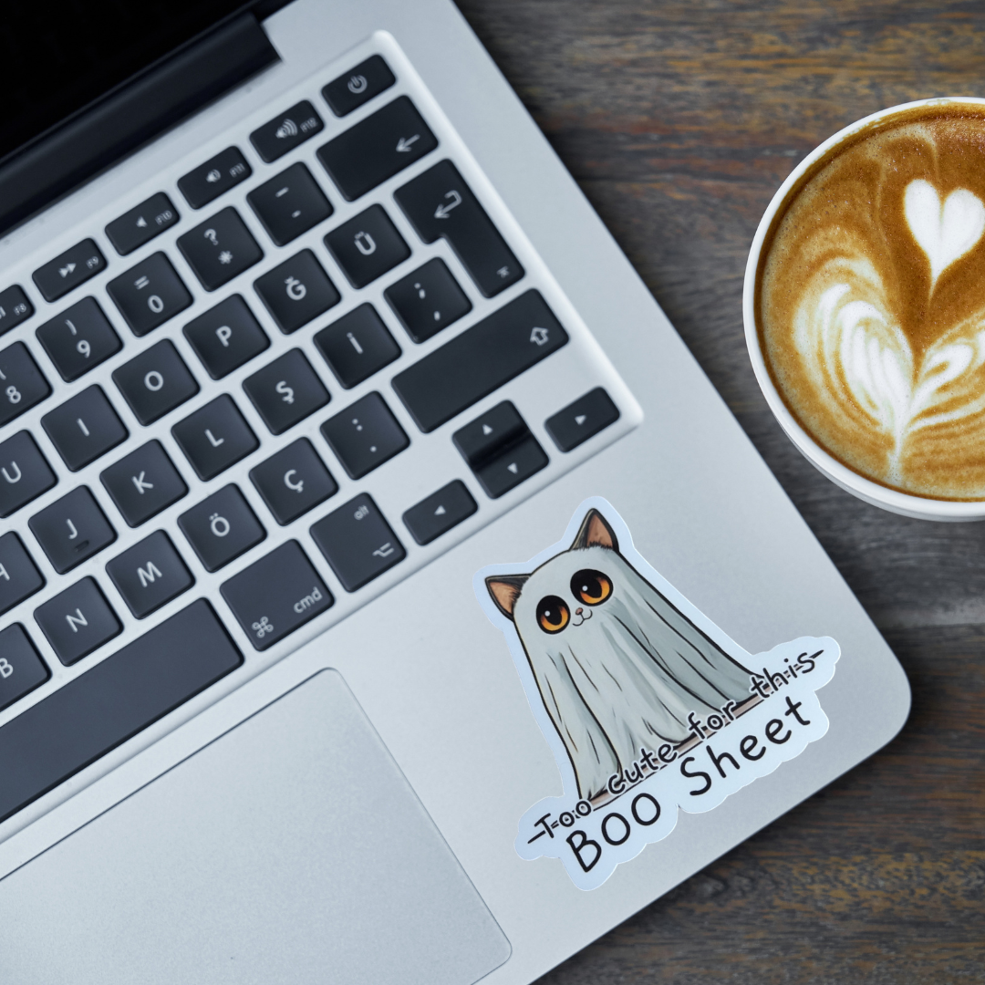 Laptop with a cat ghost sticker and a cup of coffee on a wooden surface
