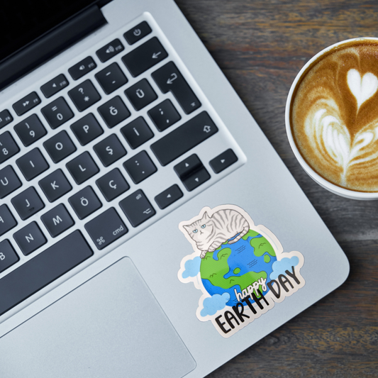 Laptop with an Earth Day cat sticker, a cup of coffee with latte art on a wooden surface