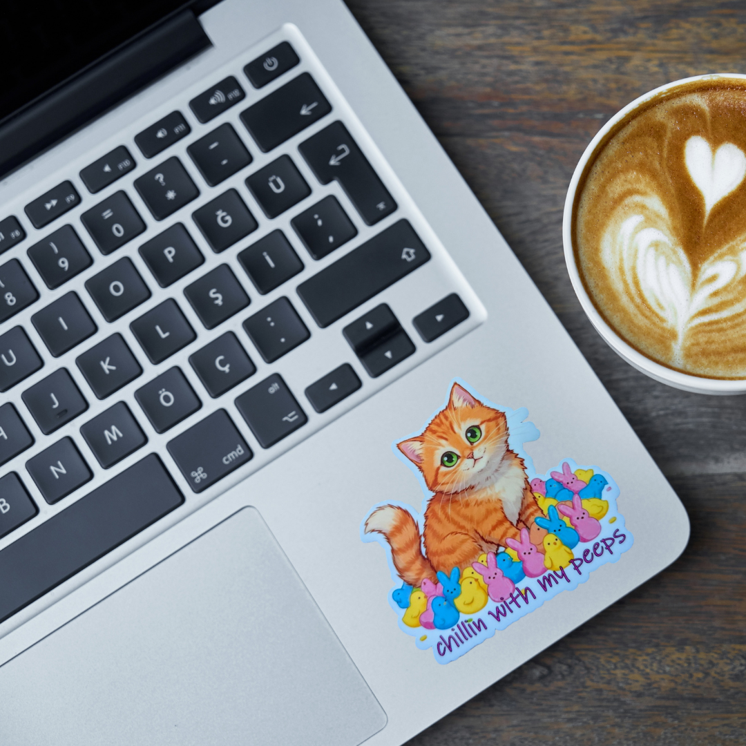 Laptop with an orange cat surrounded by peeps candy that says "chillin with my peeps" sticker and a cup of coffee on a wooden surface