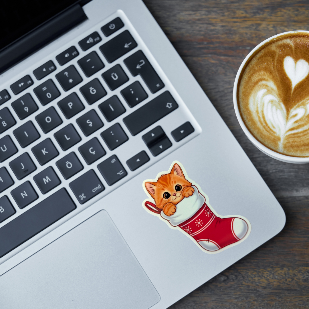Laptop with a cat in a stocking sticker and a cup of coffee on a wooden surface